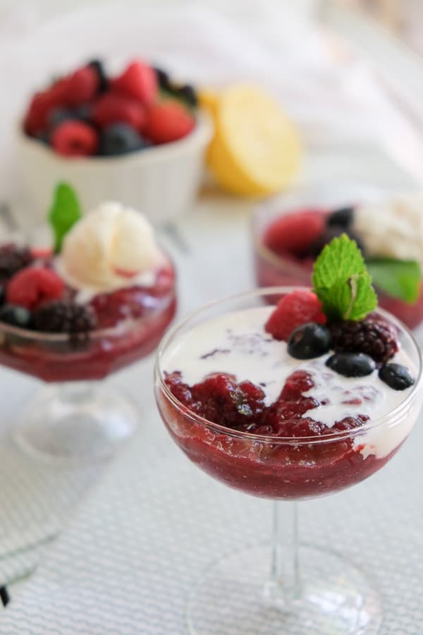 A glass of Rote Grütze or Red Berry Pudding topped with fresh berries 