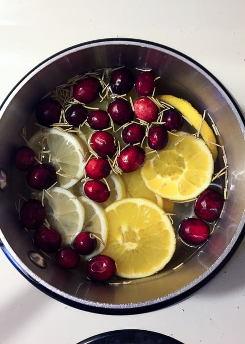 zest-less lemons and oranges on a pot of water with cloves, cinnamon stick, cranberried, and rosemary
