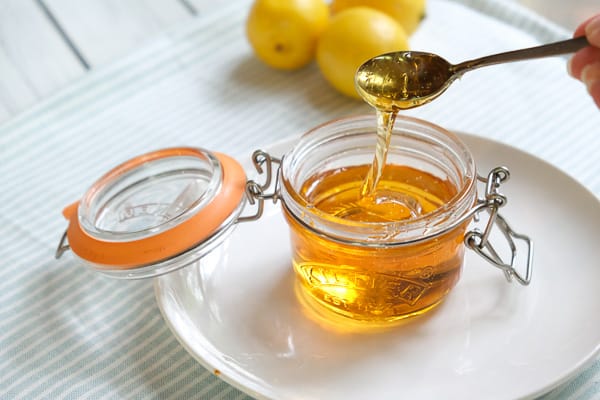 A small jar of golden syrup with lemons in the background