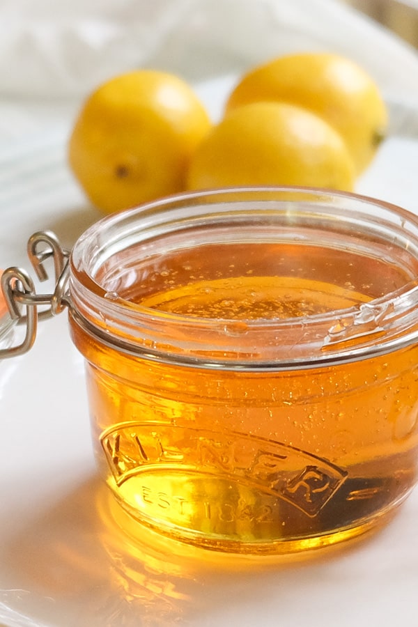 Golden syrup on a small glass jar with lemons in the background