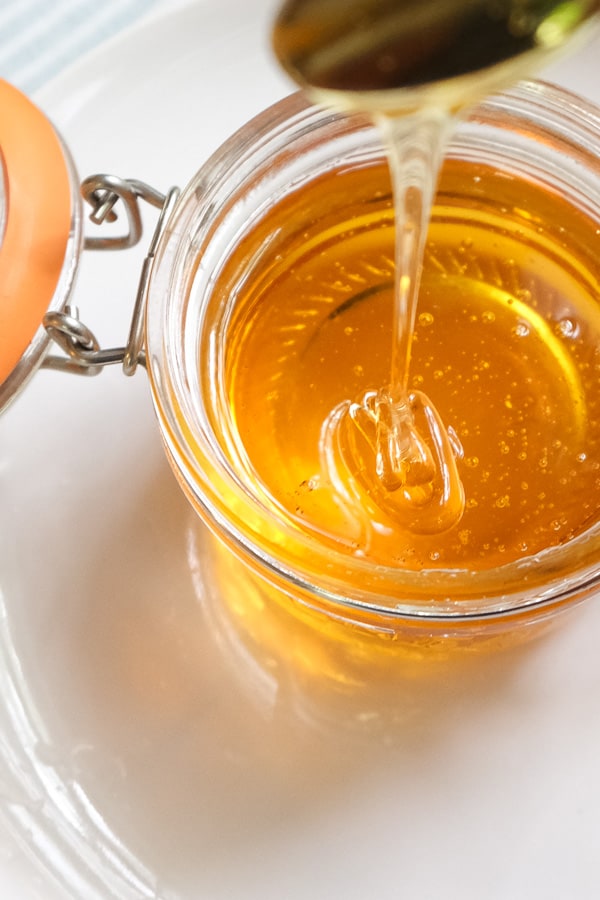 Spoonful of golden syrup drizzling down on a glass jar